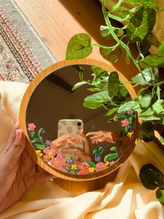 a hand holding a cell phone in front of a mirror on a table with plants