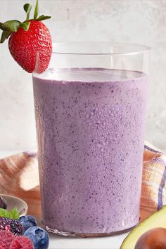 a smoothie in a glass next to some fruit and an avocado on the side