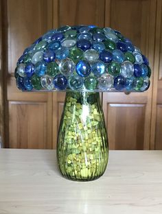 a green vase filled with lots of different colored glass beads on top of a table