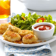 a white plate topped with fried food next to a bowl of dipping sauce and salad