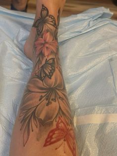 a woman's foot with tattoos on it and flowers in the middle of her leg