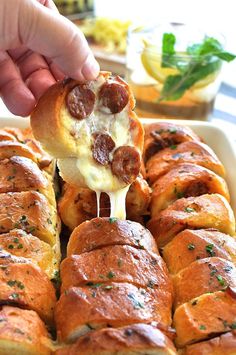 a person dipping some food into a casserole dish with cheese and pepperoni