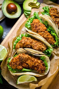 some tacos are lined up on a cutting board with limes and avocado