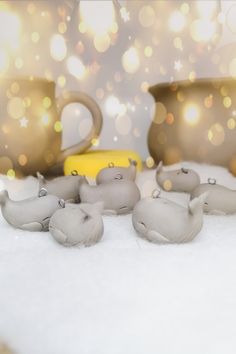 some little elephants are laying in the snow with coffee mugs and lights behind them