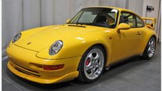 a yellow porsche parked in a garage next to a white wall and black tile floor