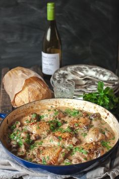 a blue pan filled with food next to bread and a bottle of wine on top of a table