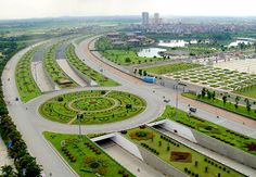 an aerial view of a city with roads and roundabouts in the foreground, surrounded by green grass