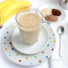 there is a drink on the plate with spoons next to it and bananas in the background