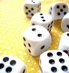 several white dices with black dots are on a yellow tablecloth and there is one in the middle