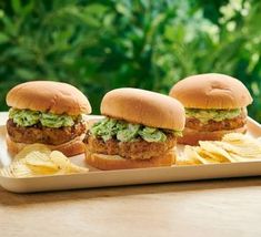 three chicken burgers with guacamole and chips on a white platter