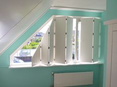 an attic bedroom with blue walls and white shutters on the window sill, along with a radiator