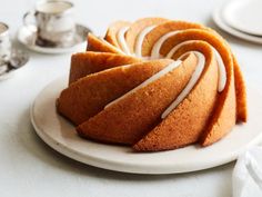 a bundt cake with white icing on a plate next to silver tea cups