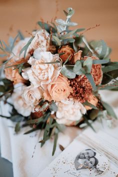 a bridal bouquet with peach flowers and greenery on the table at a wedding