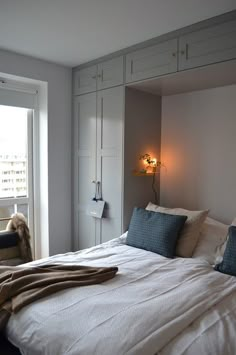 a white bed sitting next to a window in a bedroom under a light on the wall