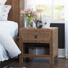 a nightstand with flowers on it next to a bed