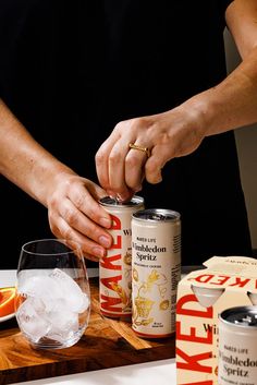 a person is holding two cans of beer on a cutting board with an orange slice