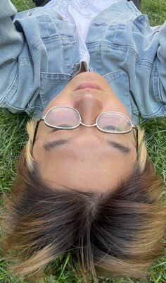 a woman laying in the grass with her head up to her face, wearing glasses