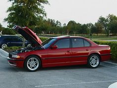 a red car with its hood open parked in a parking lot next to another car