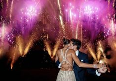 a man and woman are kissing in front of colorful fireworks at night with their arms around each other