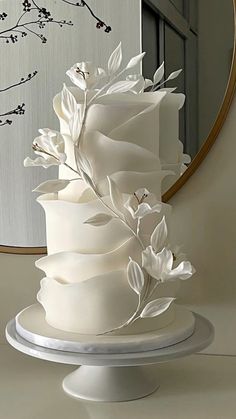 a white wedding cake sitting on top of a table in front of a round mirror