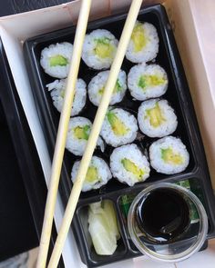 sushi with chopsticks and sauce in a black container on a table top