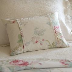 three pillows on a bed with white linens and floral print, one has pink flowers