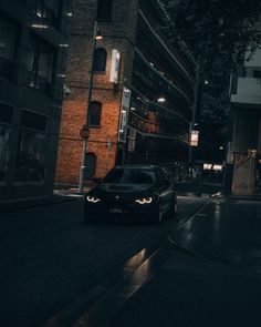 a black car parked on the side of a street at night with buildings in the background