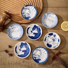 six blue and white plates with cats on them sitting on a wooden table next to sliced lemons