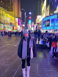 a woman standing in the middle of a city street at night with people walking around