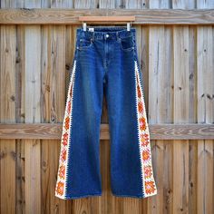 a pair of blue jeans hanging on a wooden fence with an orange and white design