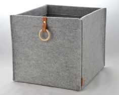 a grey felt storage box with a wooden ring on the handle and handles, sitting on a white surface