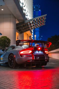 a silver sports car parked in front of a tall building with red lights on it