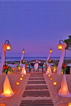 an outdoor wedding set up on the beach with candles and lanterns in front of it