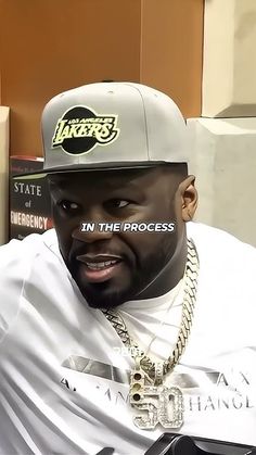 a man sitting in front of a stack of books wearing a hat with the word lakers on it