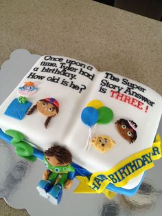 a birthday cake that is shaped like an open book with characters on it and balloons