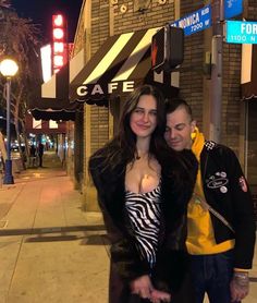 a man and woman standing next to each other in front of a building at night