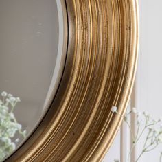 a round mirror sitting on top of a table next to a vase filled with flowers