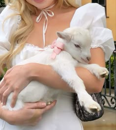 a woman is holding a baby goat in her arms while wearing a white dress and pink bow