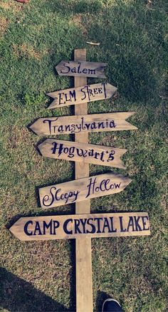 a wooden sign sitting on top of a grass covered field next to a person's feet