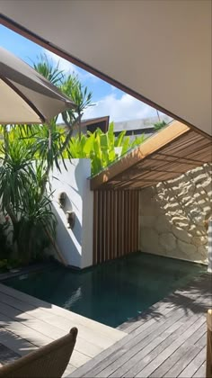 an outdoor swimming pool with wooden decking and umbrellas on the roof, surrounded by greenery