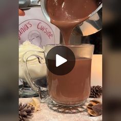 a video demonstrating how to make hot chocolate in a glass mug with a spoon pouring milk into it