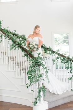 a bride standing on the stairs in her wedding dress with greenery around her waist