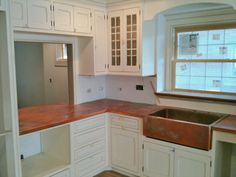 an empty kitchen with white cabinets and wood counter tops