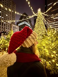 a woman wearing a red and white knitted hat standing in front of a christmas tree