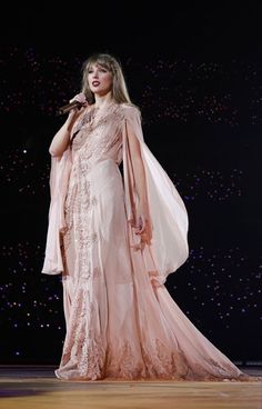 a woman in a pink dress is standing on a stage and holding a microphone to her ear