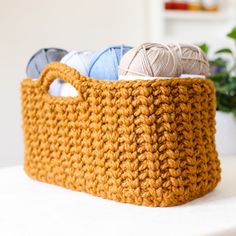 three balls of yarn are in a crocheted basket on a table next to a potted plant