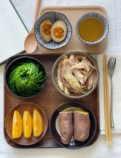 a wooden tray topped with bowls filled with food next to chopsticks and utensils