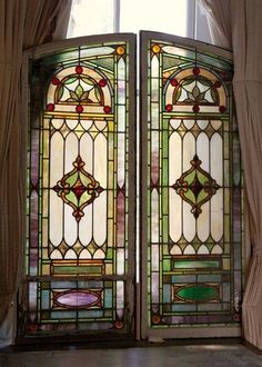 two stained glass doors are open in front of a window with curtains and drapes