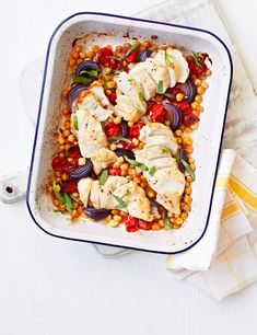 a dish filled with chicken and vegetables on top of a white table next to a napkin