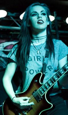 a woman with long hair and makeup playing an electric guitar in a dark room filled with lights